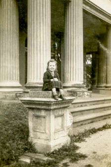 Young student sits on plinth in front of school steps 1940s